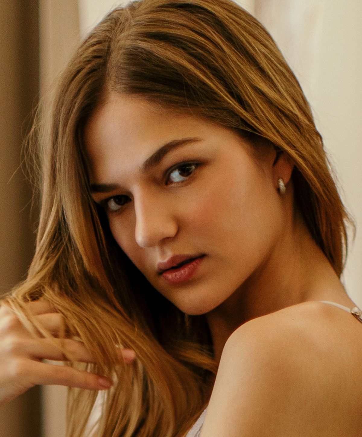 Young woman gently touching her hair, soft expression.