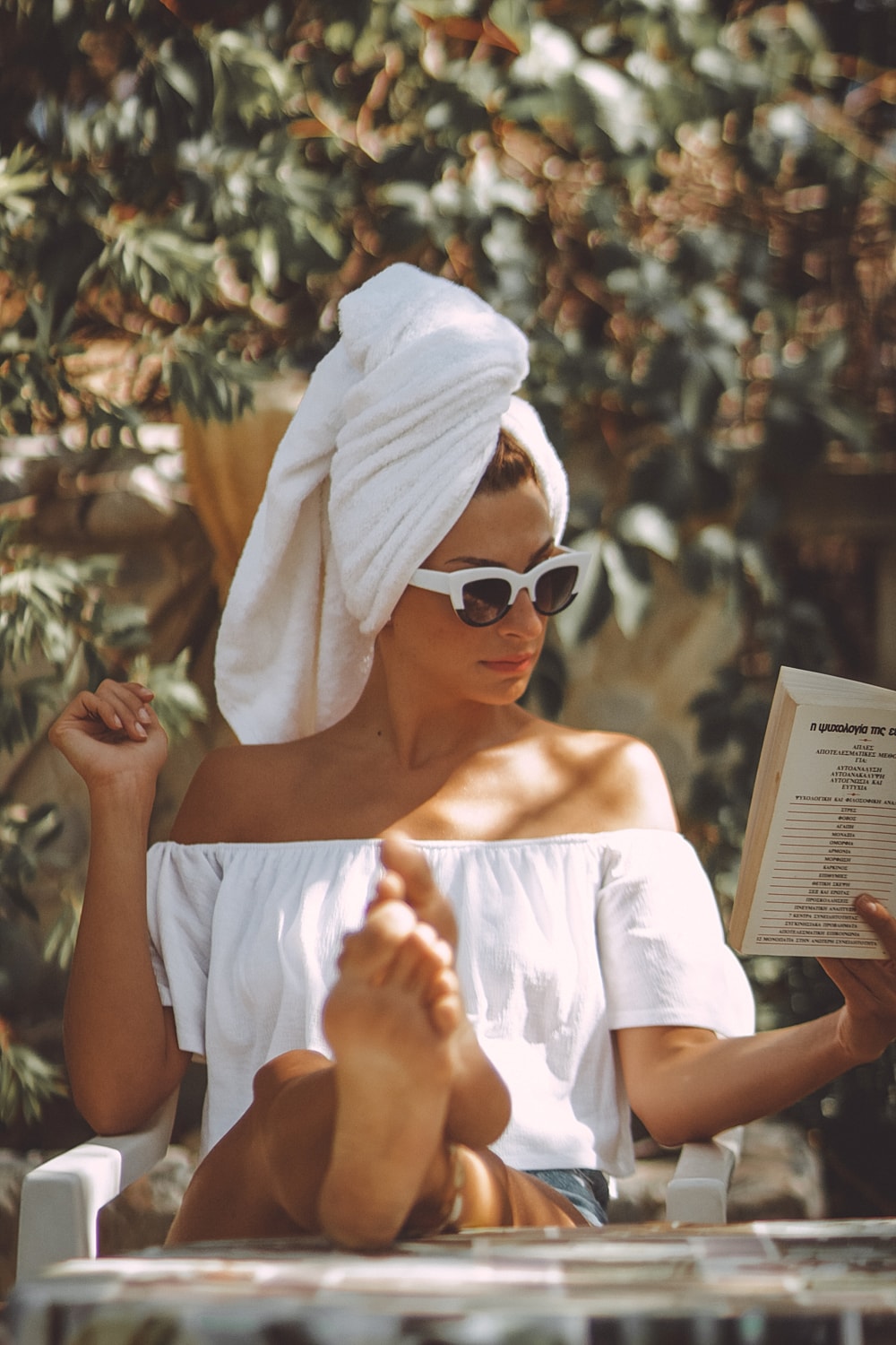 Woman reading outdoors with towel and sunglasses.