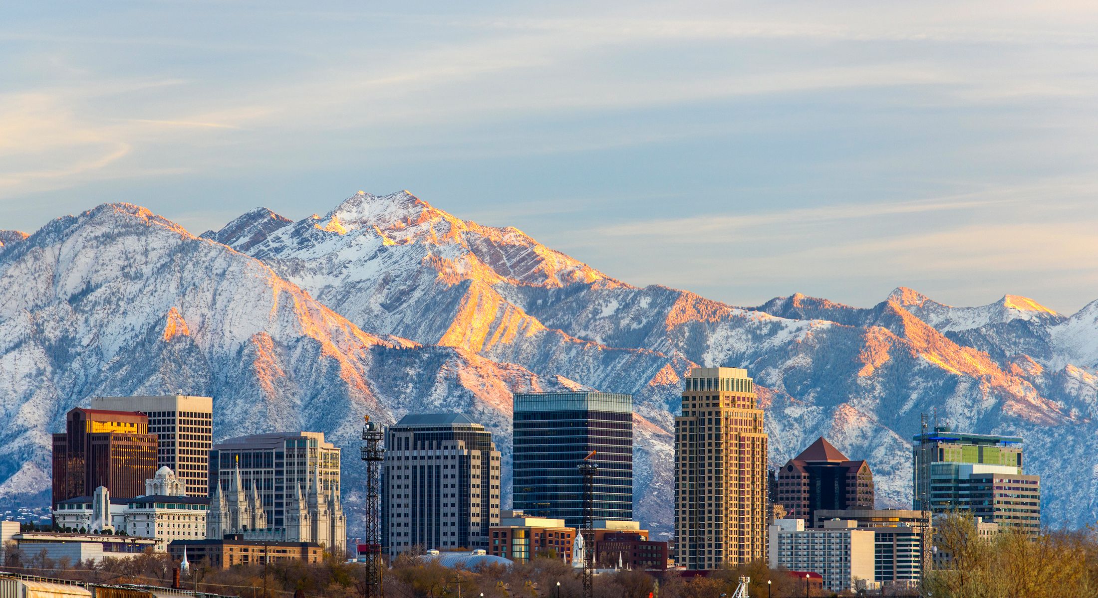 Snowy mountains behind a city skyline at sunset.