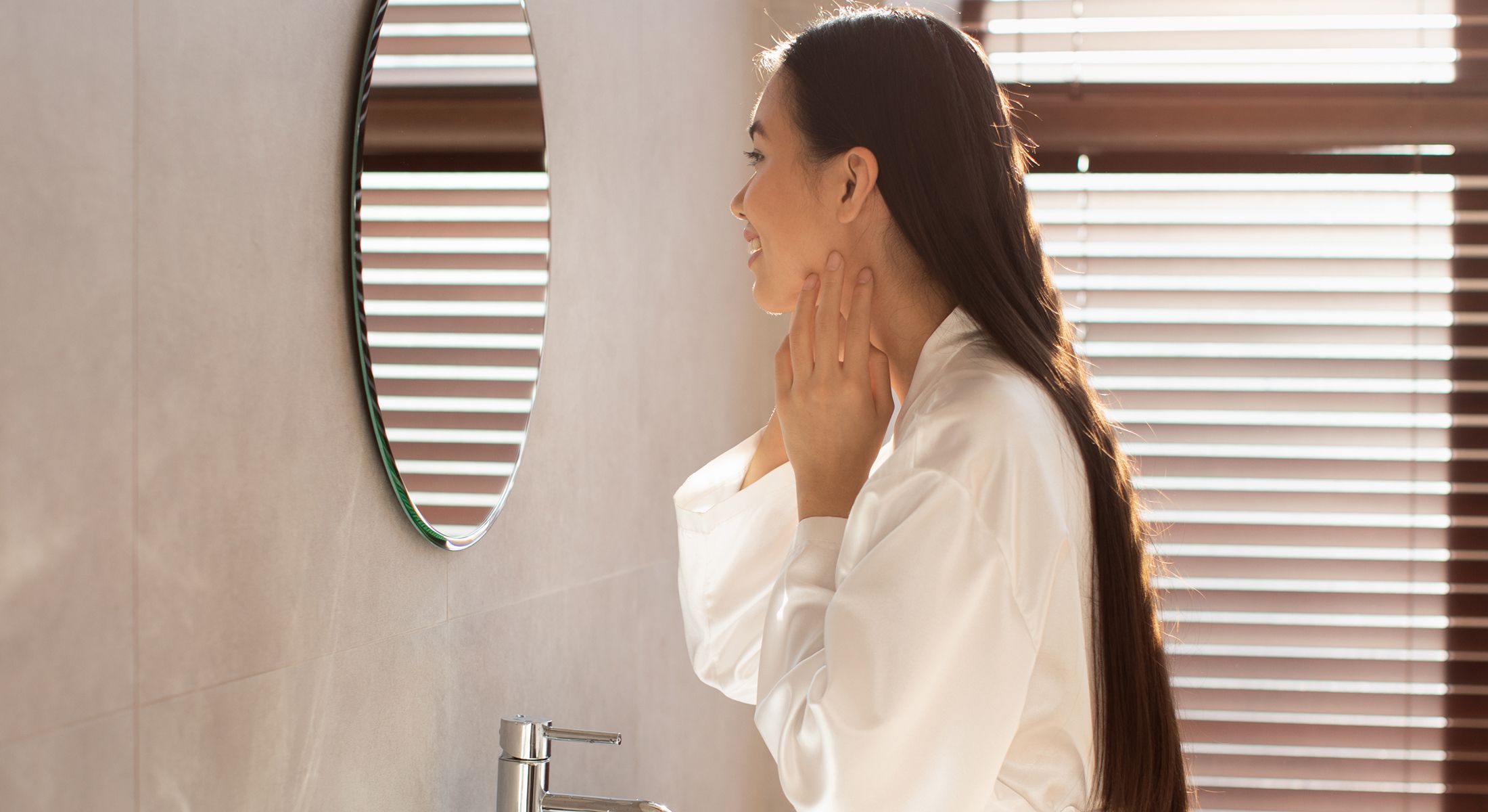 Woman in robe looking in bathroom mirror.