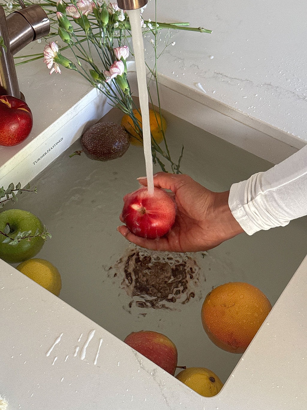 Hand washing apples in a kitchen sink.