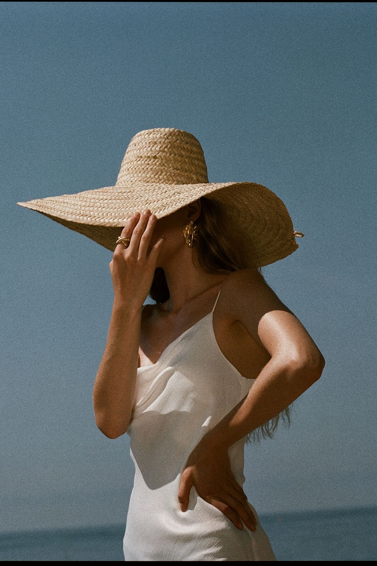 Woman in a large sunhat by the ocean.