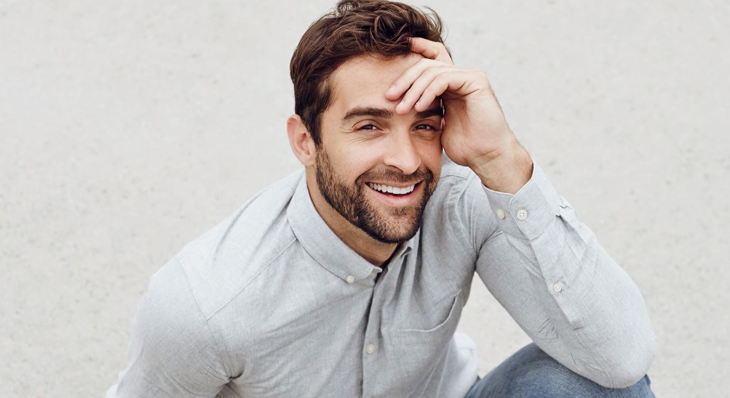 Smiling man in casual attire, hand on forehead.