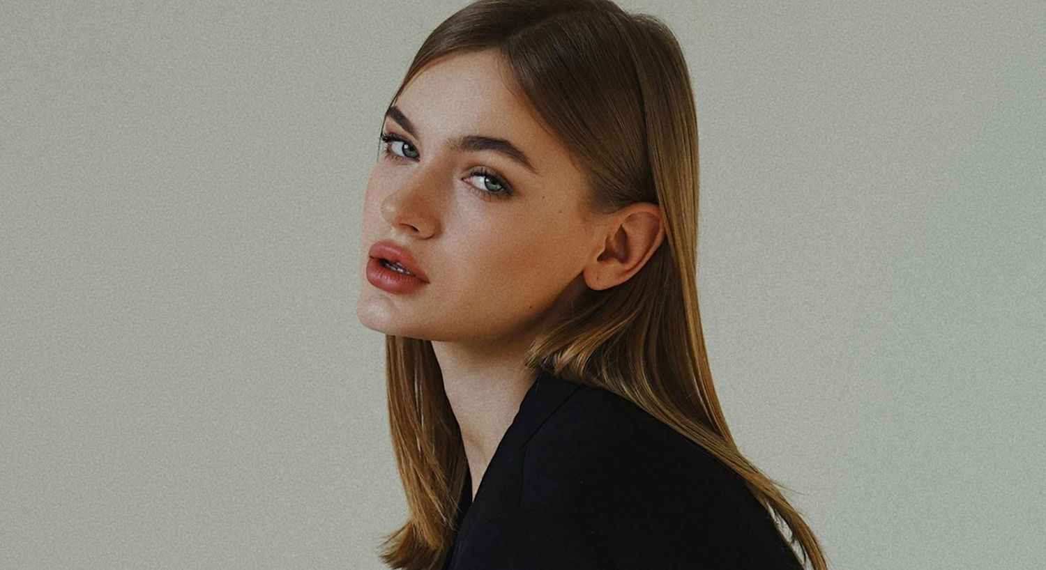 Woman with long hair, natural makeup, neutral background.